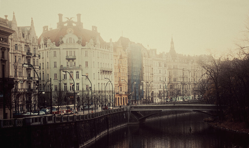 European riverside cityscape with historic architecture and bridge reflected in still water.