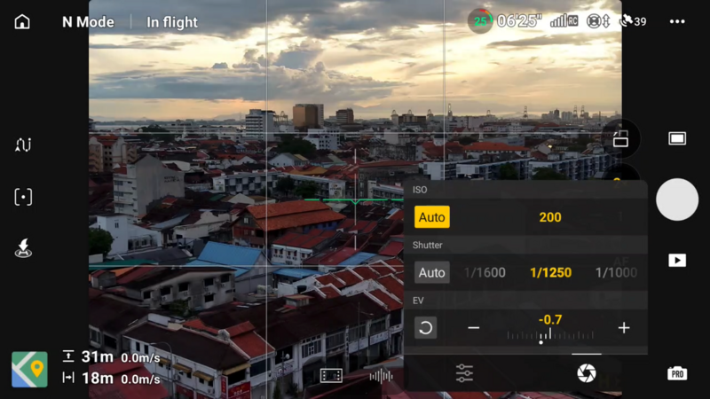 Screenshot of smartphone camera app displaying cityscape at sunset with manual exposure controls visible.