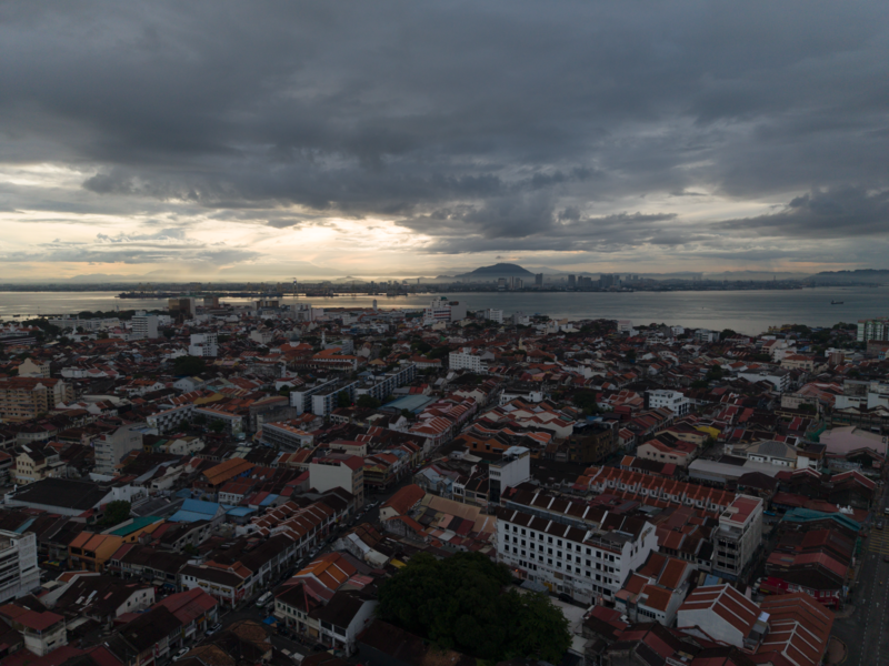 Aerial cityscape at dusk with dense residential buildings and a distant mountain across a body of water.