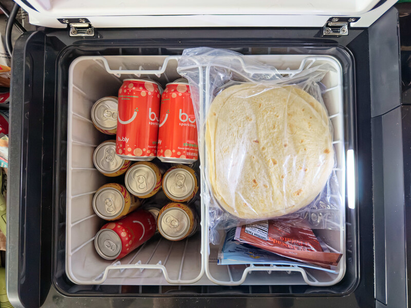 Cooler packed with beverages, condiments, and deli meat in organized compartments.