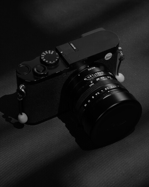 Rangefinder camera with manual lens mounted on textured surface, photographed in high-contrast black and white.