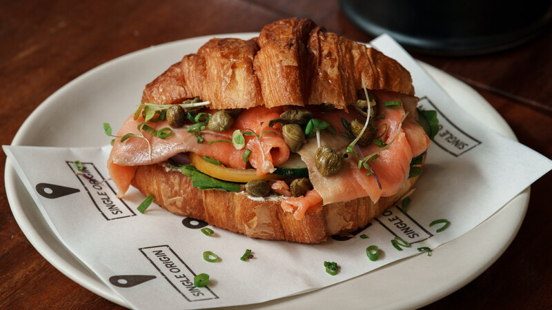 Croissant sandwich filled with smoked salmon, avocado, and microgreens on a white plate.