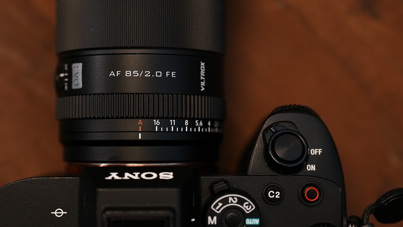 Sony mirrorless camera with AF 55/2.0 FE lens mounted, shot against warm brown background.