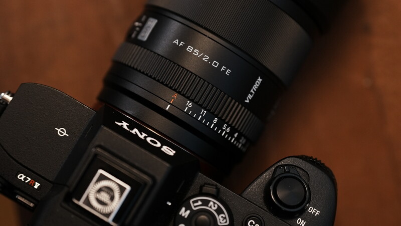 Sony mirrorless camera with AF 25/2.0 D FE lens mounted, displayed on brown leather surface.