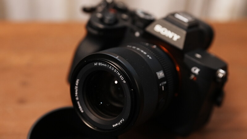 Sony mirrorless camera with 85mm lens on wooden surface, shot at shallow depth of field.