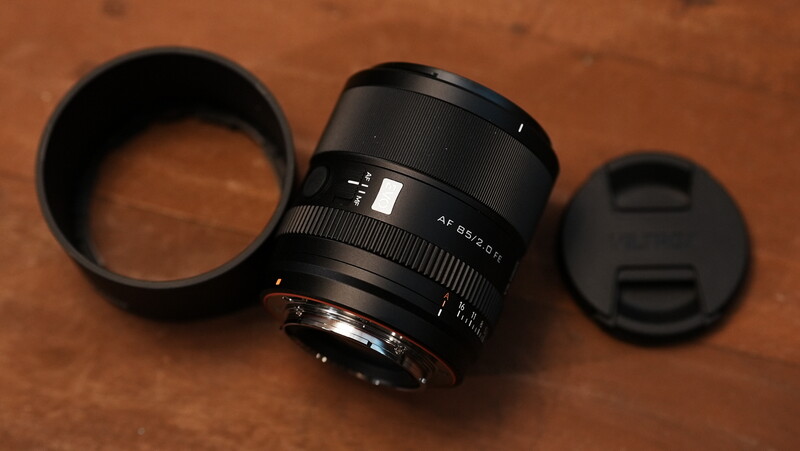 Manual focus lens with lens hood and front cap arranged on brown textured surface.