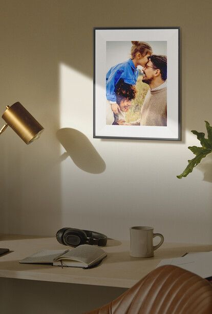 Framed portrait photograph on a wall above a minimalist desk setup with lighting and accessories.