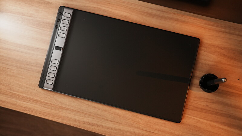 Graphics tablet with stylus pen on wooden desk surface.