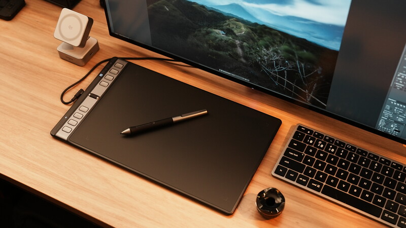 Creative workspace with graphics tablet, laptop, monitor, and stylus on wooden desk.
