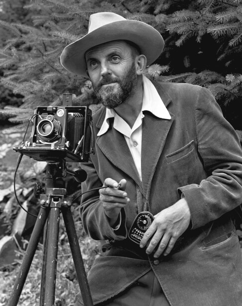 Photographer with large format camera on tripod wearing cowboy hat and coat.
