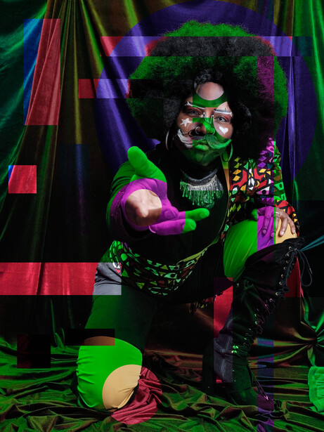 Person with afro and face paint posed under neon green and purple gels creating an otherworldly glow effect.