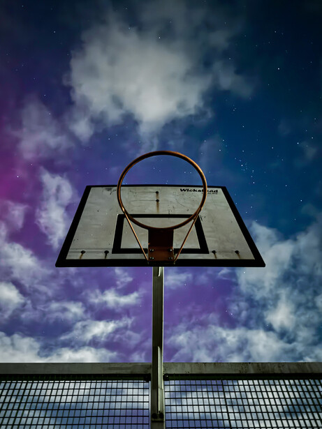 Basketball hoop and backboard photographed from below against a dramatic sky with purple and blue clouds.
