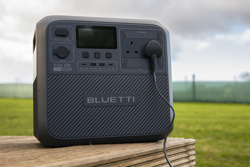 Bluetti portable power station on wooden surface with rural field and fence in background.