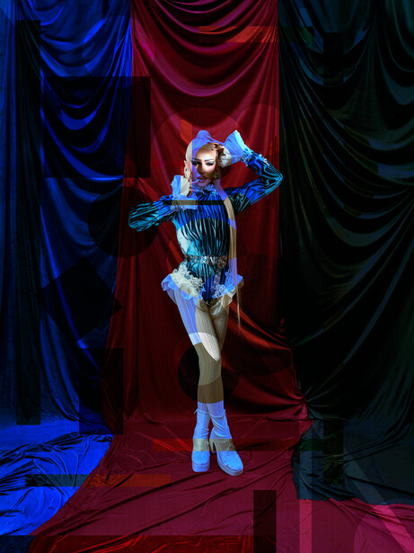 Performer in futuristic blue and silver costume striking a dynamic pose against draped fabric backdrop.
