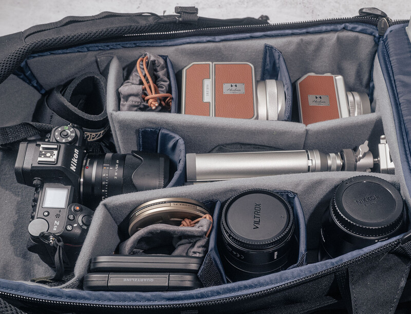 Organized camera bag interior with DSLR, lenses, filters, memory cards, and accessories neatly arranged in padded compartments.