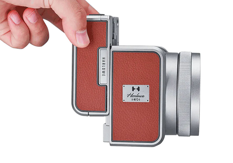 Red leather compact camera with silver metal frame and lens barrel held in hand.