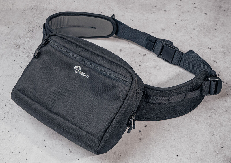 Black camera sling bag with shoulder strap displayed on concrete surface.