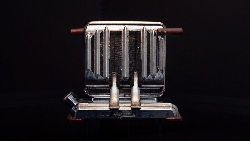 Vintage chrome toaster with dual wide slots and control levers against black background.