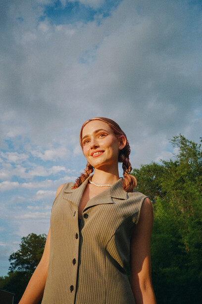 Woman with braided hair looking upward against a partly cloudy sky.