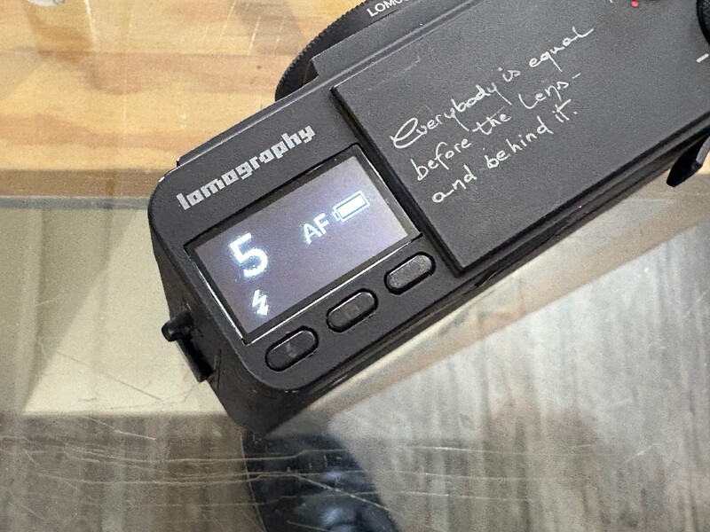 Handheld light meter displaying AF reading with handwritten notes on its case about aperture and ISO settings.