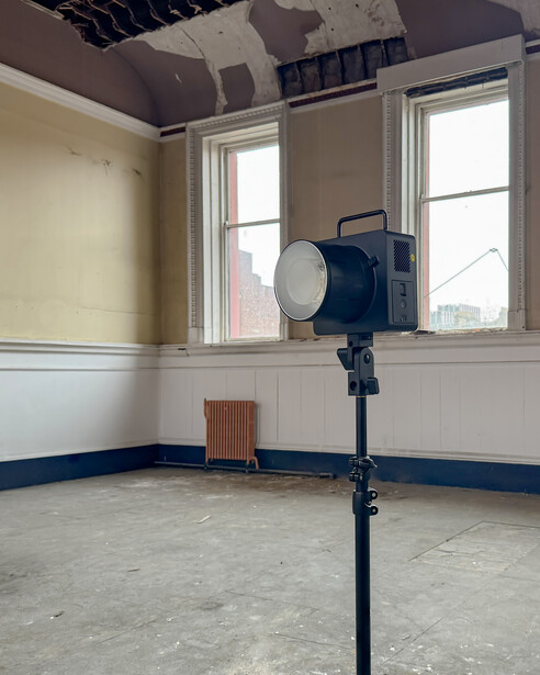 Large studio light on tripod stand positioned in empty room with two windows and two-tone painted walls.