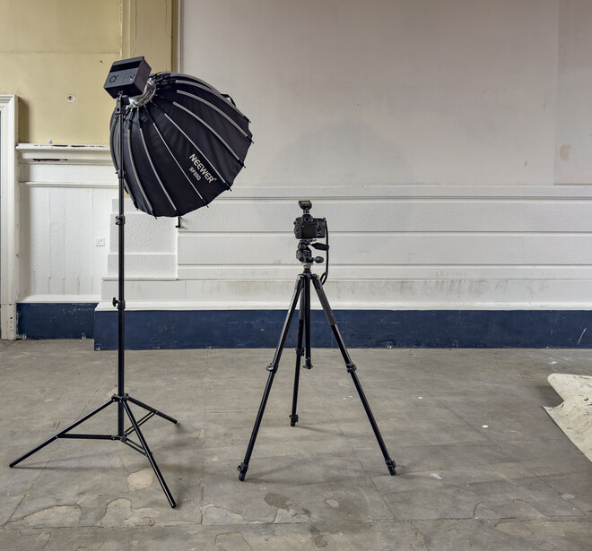 Professional studio setup with large parabolic softbox on stand and camera on tripod in empty warehouse space.