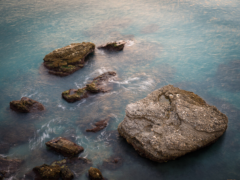 Scattered rocks and boulders partially submerged in shallow turquoise water.
