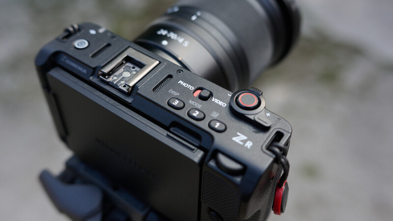 Top-down view of a compact camera showing control buttons, dial, and hot shoe with attached lens.