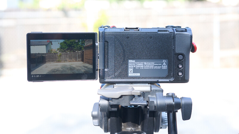 Professional video camera with articulating LCD monitor displaying backyard footage outdoors.