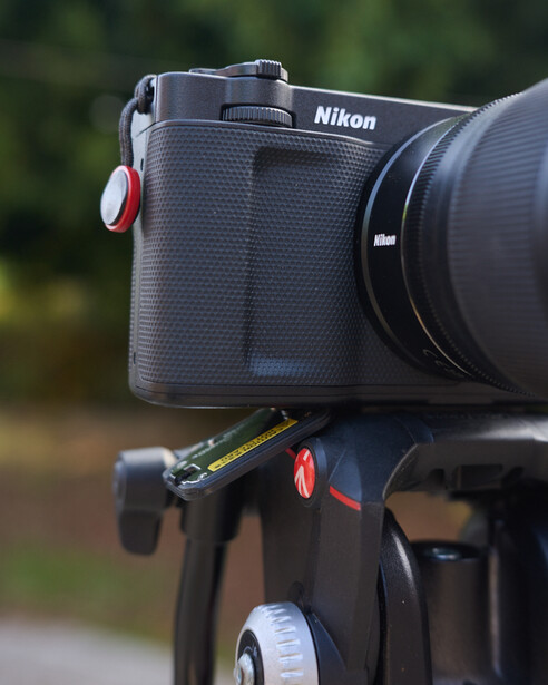 Nikon camera mounted on a tripod head with a red ball quick-release clamp and red safety lever.