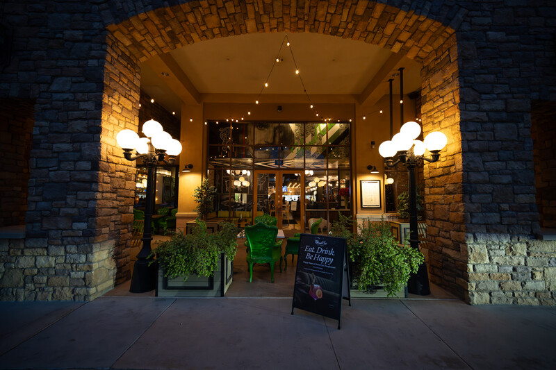 Storefront entrance with brick archway, warm interior lighting, and potted plants flanking the doors at night.