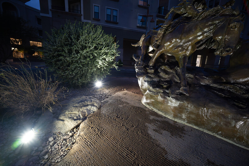 Nighttime garden courtyard with architectural stone sculpture illuminated by landscape lighting.