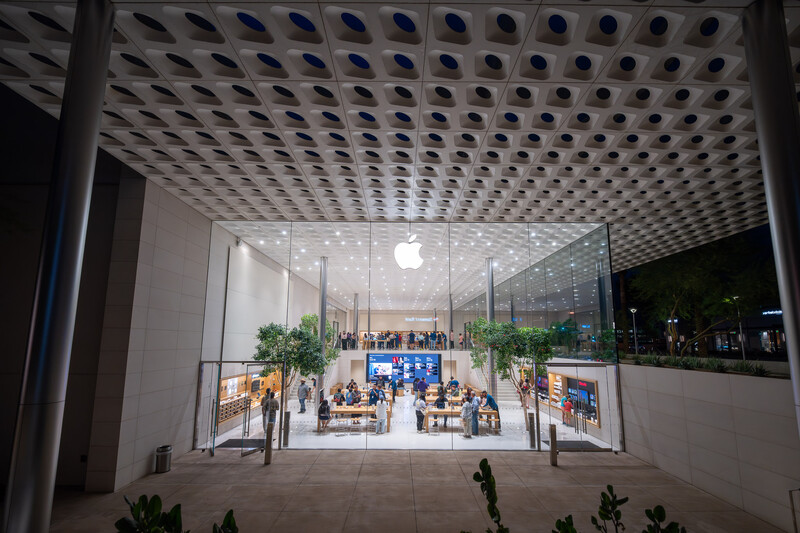 Modern Apple Store storefront at night with illuminated perforated metal ceiling and glass facade.