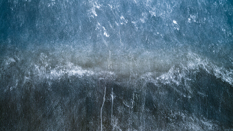 Aerial view of snow-covered forest with thin streams cutting through dense evergreen trees.
