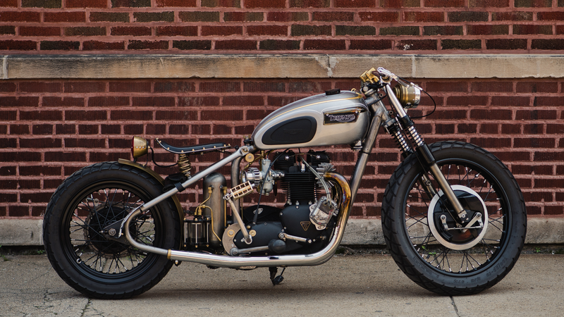 Custom motorcycle with cream tank and black engine parked against brick wall.