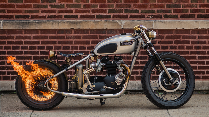Custom motorcycle with flame effects on the rear wheel against a brick wall backdrop.