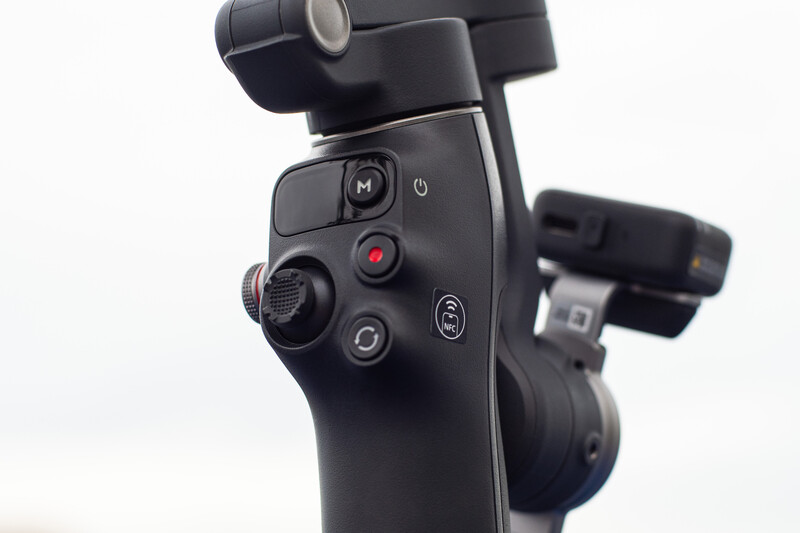 Close-up of a camera gimbal's control panel with joystick, buttons, and mode dial against white background.