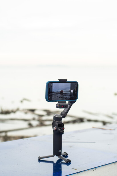 Smartphone mounted on a gimbal stabilizer with a water background slightly out of focus.