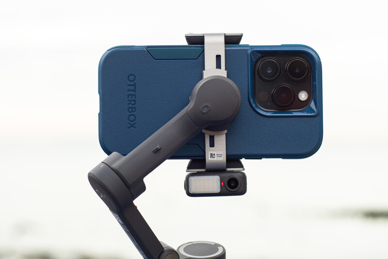 Smartphone mounted on a three-axis gimbal stabilizer with dual-lens camera visible.