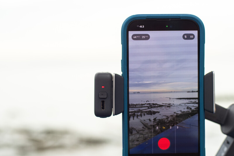 Smartphone mounted on a gimbal with external microphone, displaying a coastal landscape in the camera app.