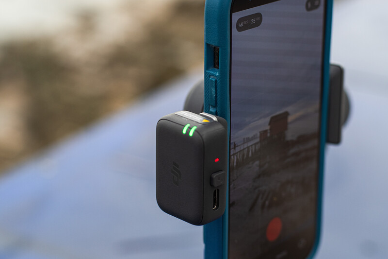 Smartphone mounted on a blue rig with a compact wireless microphone attachment clipped to the side.