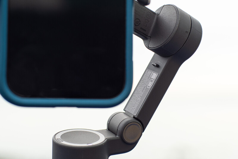 Handheld gimbal stabilizer with smartphone mounted on articulating arm against white background.