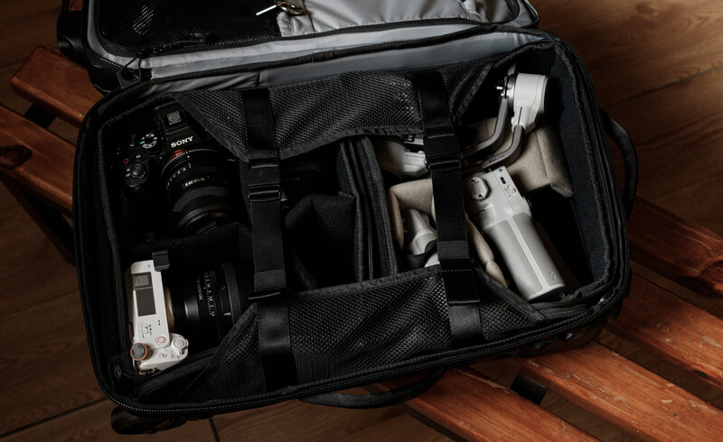 Open camera bag displaying organized photography gear including a DSLR camera, lenses, and accessories on a wooden surface.