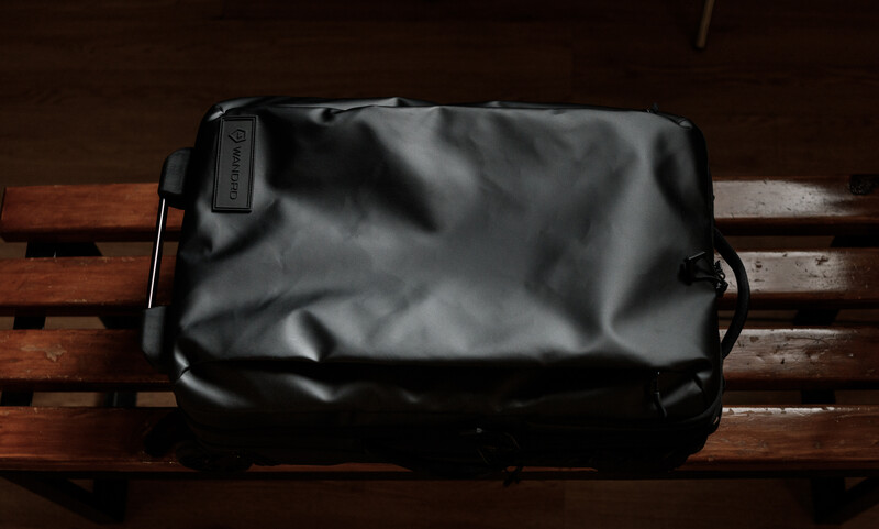 Black waterproof camera bag resting on wooden bench slats with handle and attachment point visible.