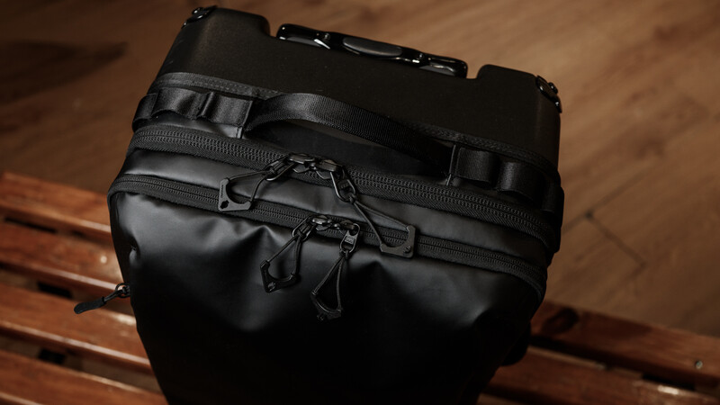 Black tactical backpack with multiple zippered compartments and straps on wooden floor.