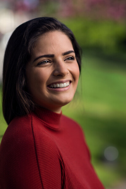 Woman in red long-sleeve shirt smiling at camera with blurred green background.