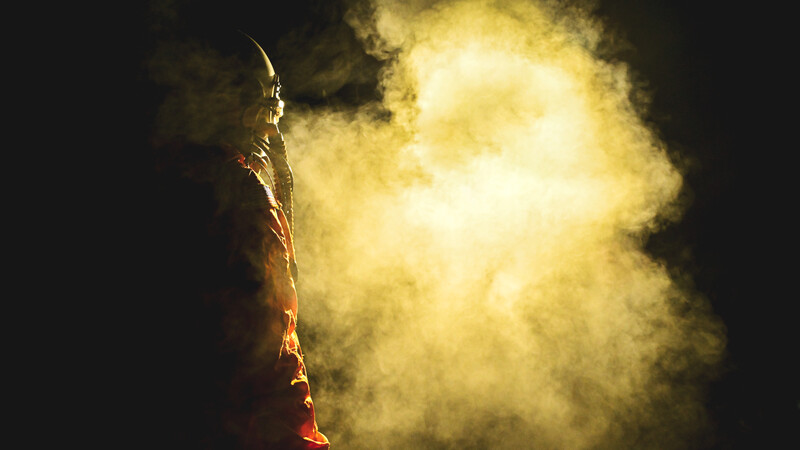A figure silhouetted against a bright explosion of yellow and orange light and smoke against a dark sky.