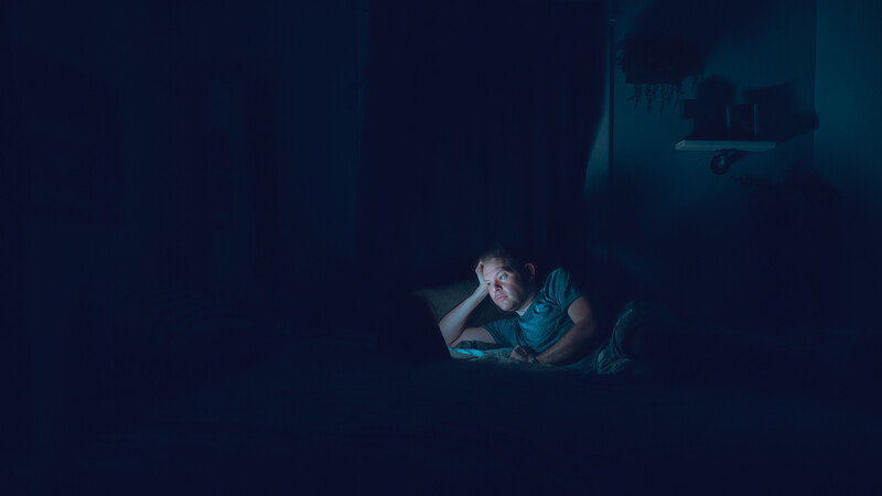 Person illuminated by smartphone screen in dark environment.