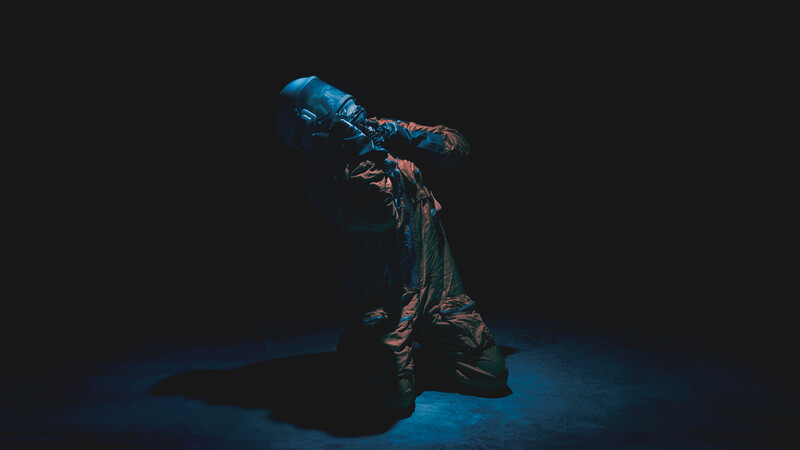 Person in dramatic pose against dark background, illuminated by blue and warm amber stage lighting.
