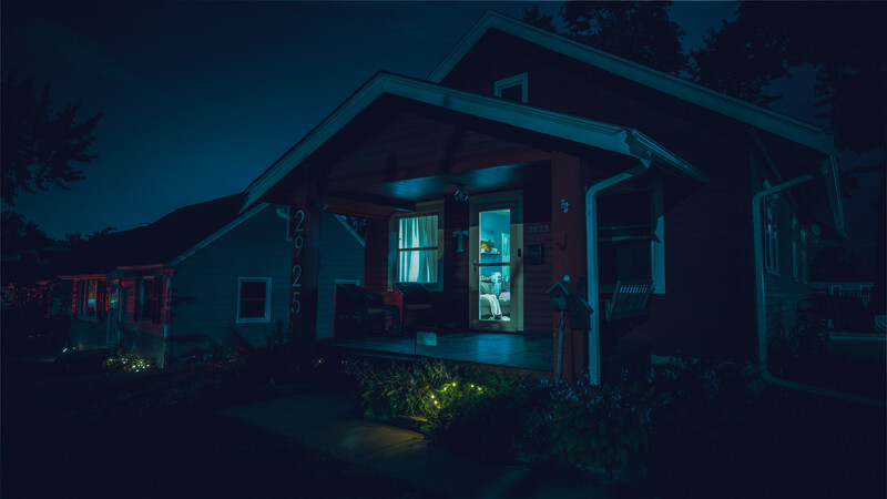 Small residential house at night with warm interior lighting glowing through windows against deep blue twilight sky.
